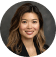 Portrait of a smiling Asian woman with long brown hair, wearing a green blouse, set against an industrial maintenance workshop background.