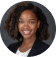 Professional headshot of a smiling young woman with shoulder-length curly hair, wearing a dark industrial maintenance uniform blazer.
