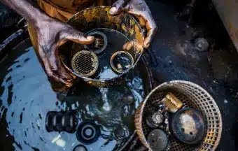 A person cleans mechanical parts in a container of water, with focus on their hands and the components immersed in the dark liquid.