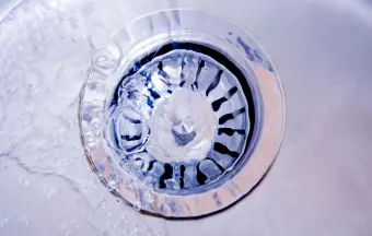 Water flowing down a shiny metal sink drain with visible swirl patterns.